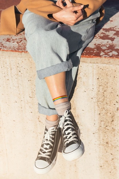 Foto piernas laterales de mujer con pulsera de arco iris del orgullo gay lgbtqi con jeans enrollados