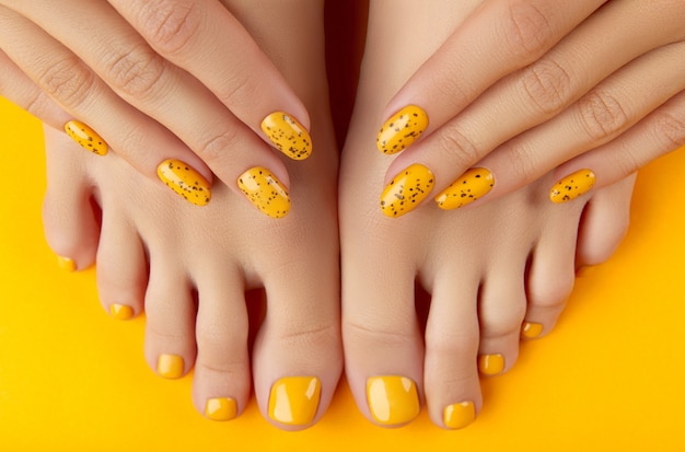 Piernas y manos femeninas con diseño de uñas de verano sobre fondo naranja