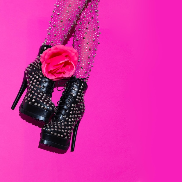 Piernas de moda y rosas en botas negras de tacón sobre fondo rosa mínimo