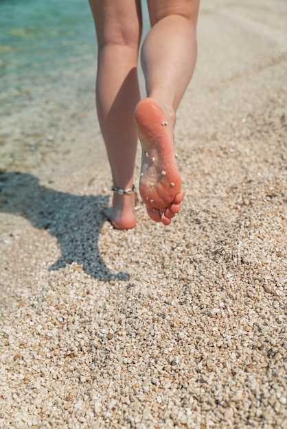 Piernas de mujer caminando descalzo por vacaciones de verano en la playa del mar
