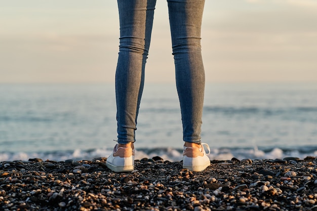 Foto piernas de mujer irreconocible en la arena de la playa al atardecer.