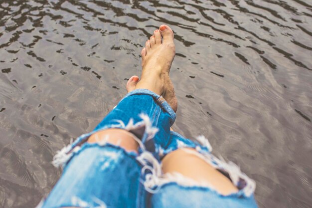 Piernas de mujer con jeans rasgados azules sobre el agua en el parque de la ciudad