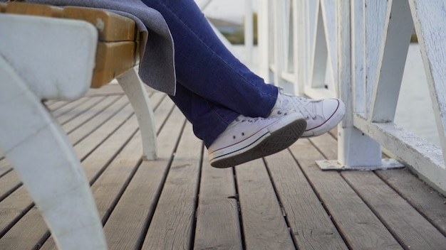 Las piernas de una mujer sentada en un banco del parque en zapatillas blancas