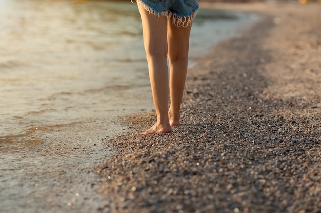 Piernas de mujeres caminando en la playa al atardecer.