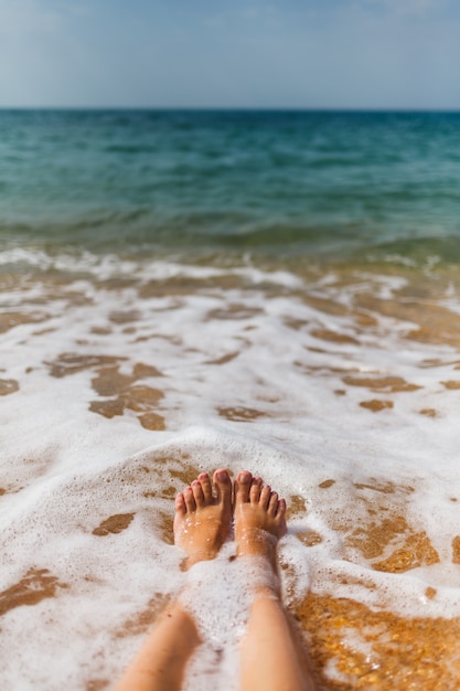 Piernas de la niña en el agua de mar en la orilla arenosa