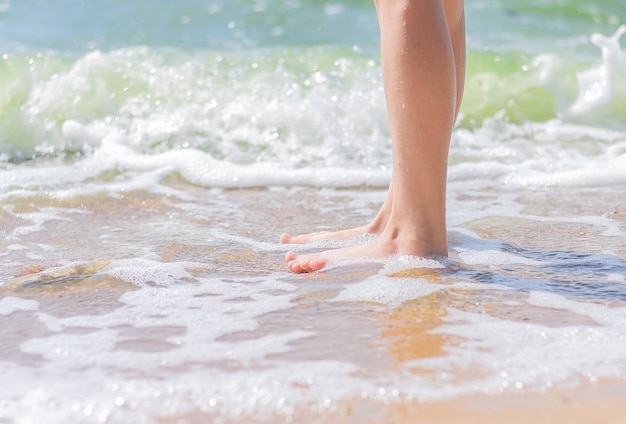 Las piernas de una niña están de pie en el agua cerca de la orilla del mar. concepto de vacaciones de verano