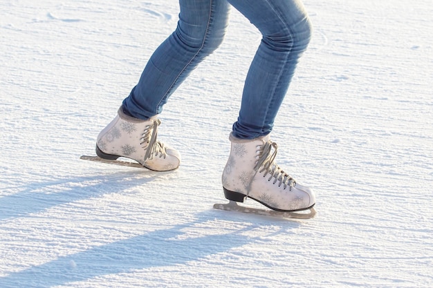 Piernas de una niña en jeans y patines blancos en una pista de hielo