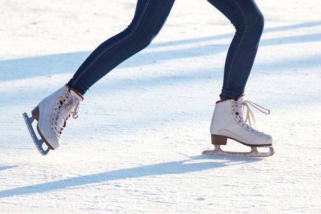 Piernas de una niña en jeans y patines blancos sobre un anillo de hielo