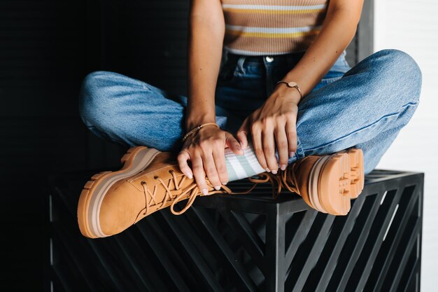 Piernas de una niña en jeans y zapatos marrones sentados en un pedestal de metal Temporada invierno verano