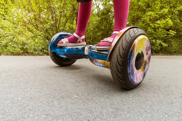 Piernas de niña montando en mini hoverboard autoequilibrado en el parque de la ciudad. Scooter electrónico al aire libre: transporte ecológico portátil personal, scooter giroscópico, hyroscooter, rueda de equilibrio inteligente, mini segway