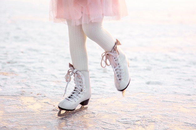 Piernas de niña patinando sobre hielo en la luz del atardecer por la noche