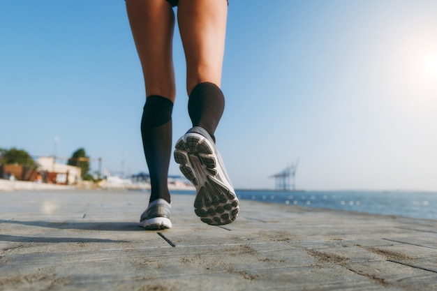 Las piernas de la niña con polainas negras y zapatillas grises, que corre por la mañana al amanecer cerca del mar.