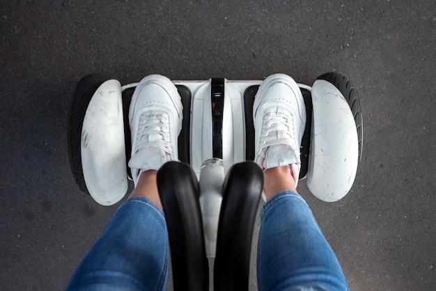 Piernas de una niña en zapatillas blancas sobre un hoverboard blanco en un primer plano del parque