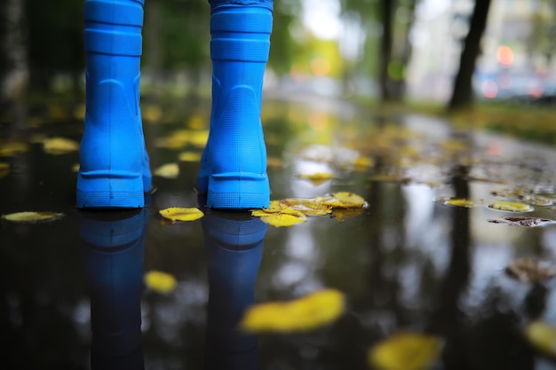 Piernas de niño con botas de goma azules saltando en los charcos de otoño