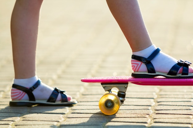 Piernas del niño en patineta de plástico rosa