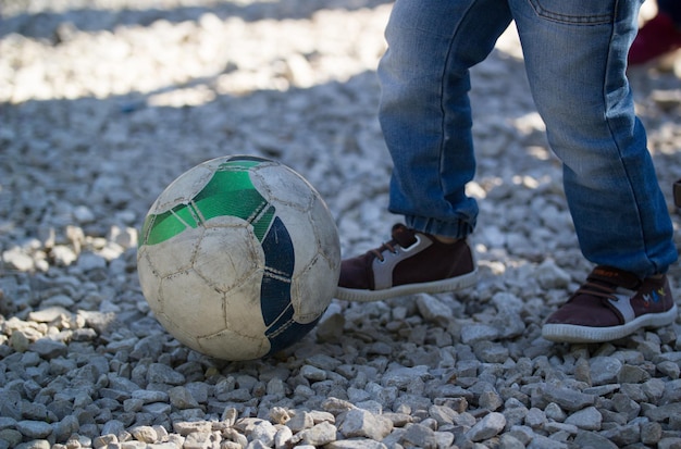 Piernas de niño pequeño patea una pelota de fútbol al aire libre en un día soleado