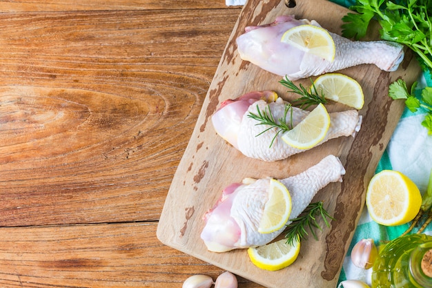 Piernas de pollo sin cocer crudas, baquetas en el tablero de madera, carne con ingredientes para cocinar