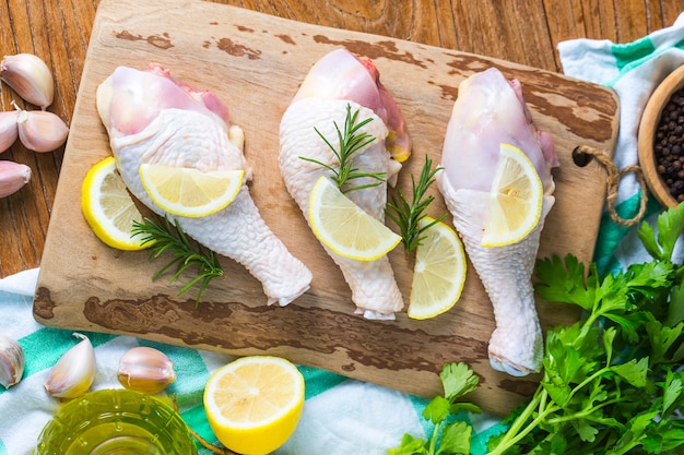 Piernas de pollo sin cocer crudas, baquetas en el tablero de madera, carne con ingredientes para cocinar