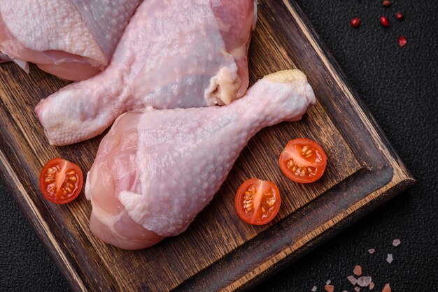 Piernas de pollo crudas con especias saladas y hierbas sobre un fondo de hormigón oscuro