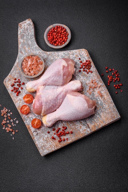 Foto piernas de pollo crudas con especias saladas y hierbas sobre un fondo de hormigón oscuro