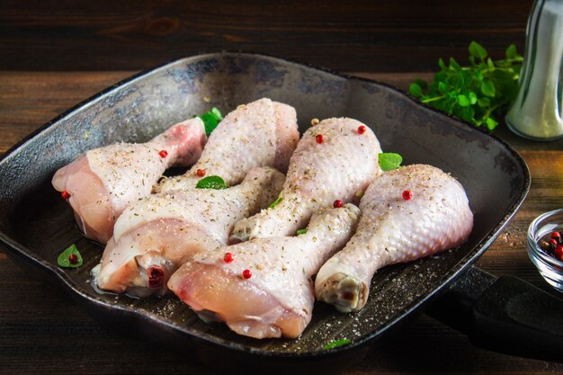 Piernas de pollo crudas en un sartén en una tabla de madera. Ingredientes de carne para cocinar.