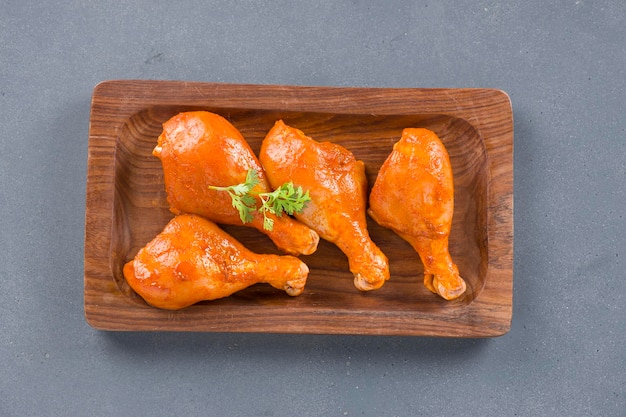 Piernas de pollo marinadas crudas o baquetas dispuestas en una base de madera adornadas con hojas de cilantro frescas que se colocan sobre un fondo de textura gris.