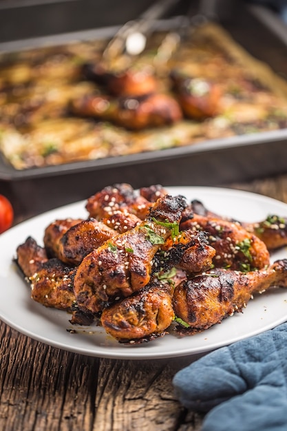 Piernas de pollo a la parrilla BBQ con especias, hierbas y sésamo sobre papel horneado. Harina de ave asada en plato blanco.