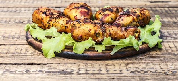 Piernas de pollo a la parrilla y hojas de lechuga en tabla de cortar de madera y superficie de madera