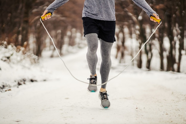 Piernas saltando la cuerda en camino nevado en invierno. Deporte de invierno, ejercicios cardiovasculares, hábitos saludables.