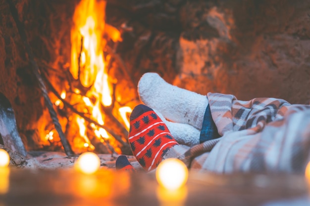 Piernas de sección baja de marido y mujer cubiertas de calcetines y una manta cálida relajándose frente a la chimenea ardiente durante las vacaciones de Navidad de invierno Par de pies en calcetines de lana junto a la chimenea de Navidad