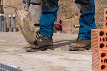 Piernas de los en el sitio de construcción con una pala botas de seguridad y ladrillos | Foto Premium