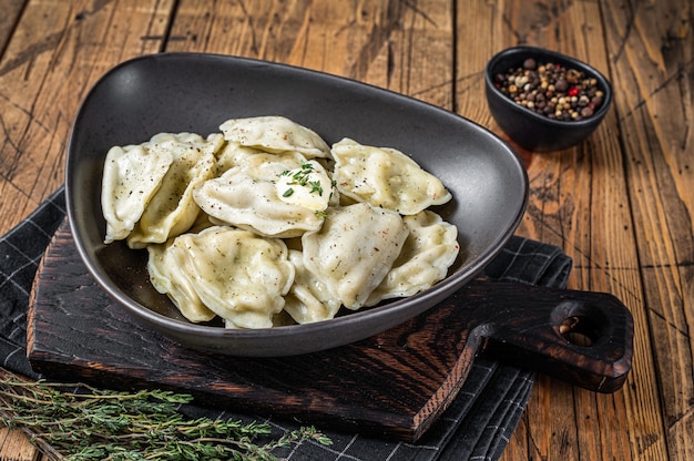 Pierogi de bolinhos de massa com batata em um prato com ervas e manteiga. Fundo de madeira. Vista do topo.