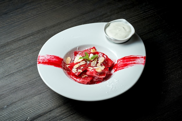 Pierogi ou Varenyky ucraniano clássico com cerejas, molho vermelho, creme de leite e amêndoas em um prato branco.