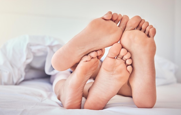 Los pies se aman y una pareja en la cama para relajarse por la mañana mientras se unen en su hogar por confianza o apoyo Dormitorio durmiendo o soñando con un hombre y una mujer descansando bajo una manta en una casa