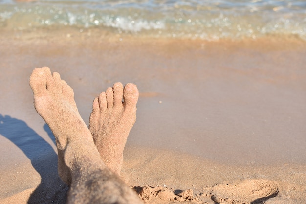 Pies en la arena en la playa contra un mar azul