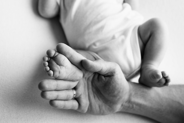 Pies de bebé en manos de madre padre hermano mayor o hermana familia Pies de un pequeño recién nacido de cerca Pies de niños pequeños rodeados por las palmas de la familia Blanco y negro