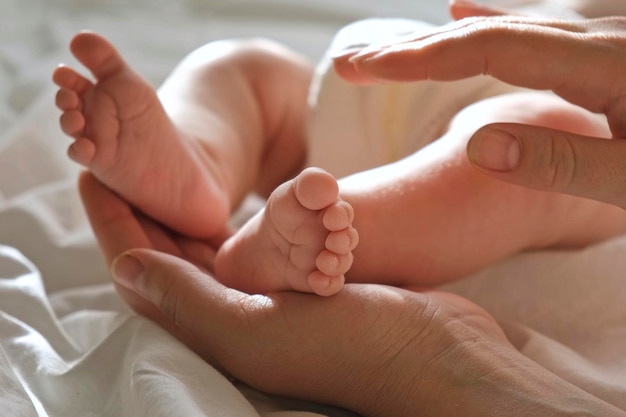 Pies de bebé en las manos de la madre en la palma de su mano Padres felices sosteniendo los pies de su bebé de cerca Concepto de nacimiento de la familia de maternidad Mujer tocando las piernas del bebé Pie pequeño de la mamá recién nacida y su hijo