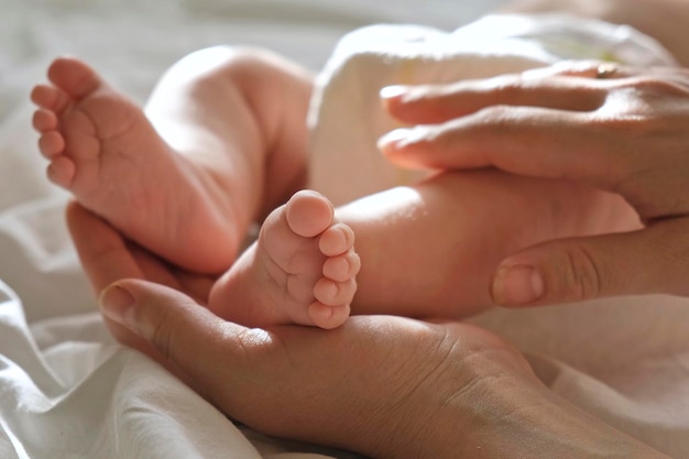 Pies de bebé en las manos de la madre en la palma de su mano Padres felices sosteniendo los pies de su bebé de cerca Concepto de nacimiento de la familia de maternidad Mujer tocando las piernas del bebé Pie pequeño de la mamá recién nacida y su hijo