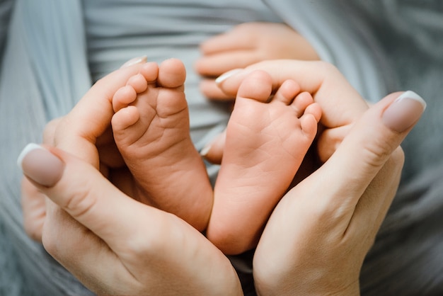 Pies del bebé recién nacido en manos femeninas, con forma de corazón encantador