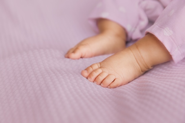 Foto pies del bebé recién nacido en tela lila, primer plano de pies descalzos infantiles en un enfoque selectivo,