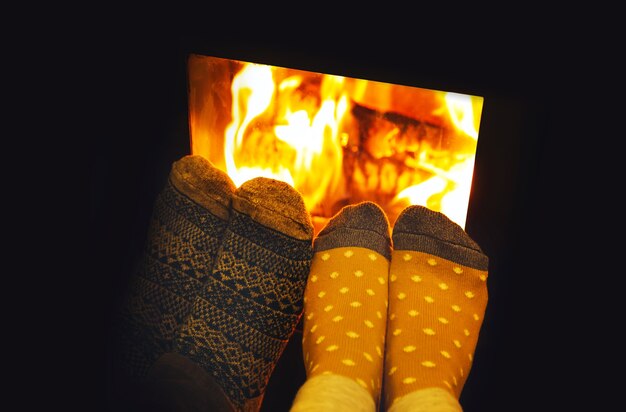 Pies en calcetines de lana de amantes de la pareja calentando por fuego acogedor