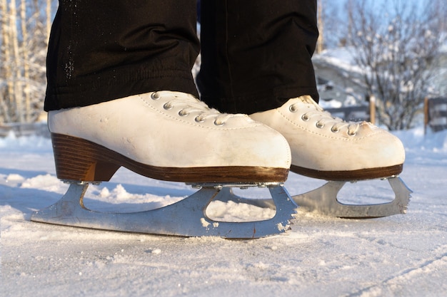 Pies de una chica que llevaba patines de pie sobre una pista de hielo en el campo en un día soleado de invierno