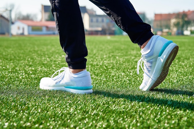 Pies de corredor masculino con zapatillas blancas en el estadio con hierba verde de cerca Zapatillas deportivas para correr Fitness y concepto de estilo de vida saludable