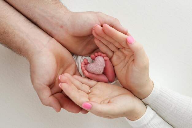 Pies dedos de los pies talones de un recién nacido Pie infantil en manos de madre padre padres con un corazón rosa tejido Las piernas del niño en brazos de mamá y papá Sobre un fondo blanco