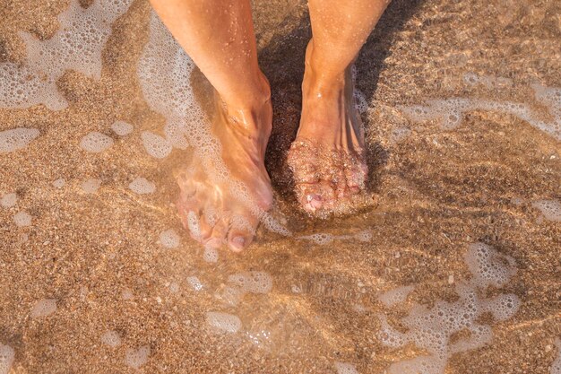 Los pies descalzos femeninos se paran en el mar en una playa de arena Vista superior plana