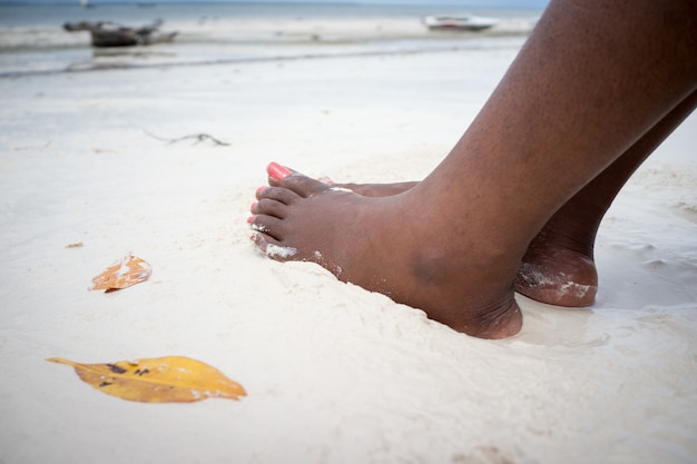 Pies femeninos africanos en la arena de la playa