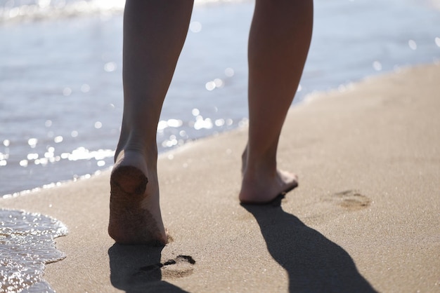 Pies femeninos descalzos caminando por la playa de mar closeup