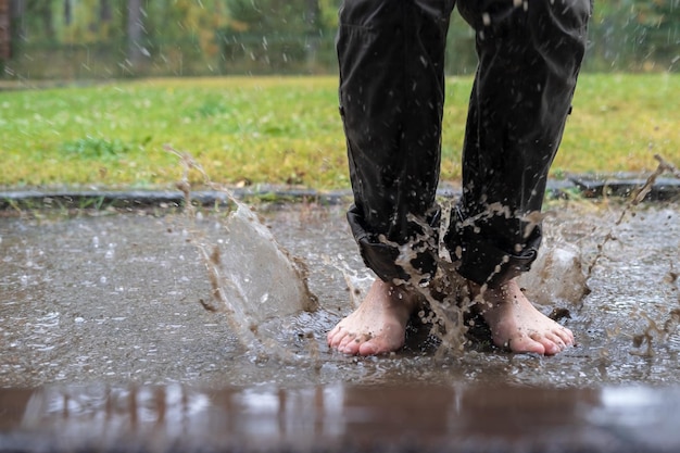 Los pies femeninos descalzos saltan en un charco después de que la lluvia rocíe agua sucia en diferentes direcciones