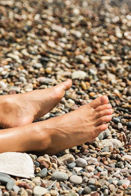 Pies femeninos durante el día soleado en la playa de guijarros