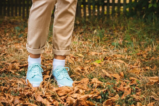 Los pies femeninos en pantalones beige y unas zapatillas turquesa están en las hojas caídas